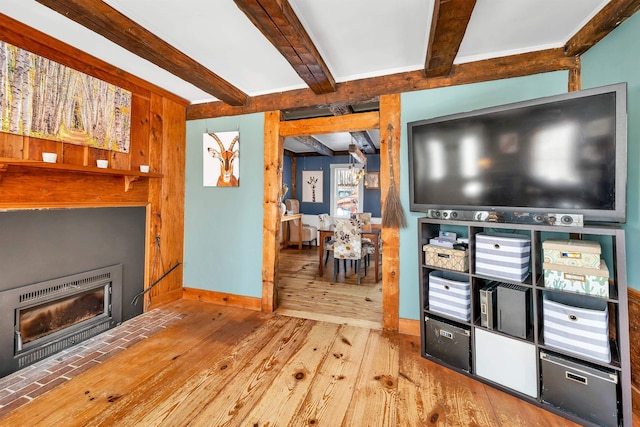 living area featuring light wood-type flooring, beamed ceiling, a fireplace, and baseboards