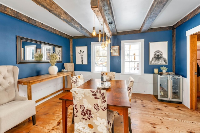 dining area with light wood-style floors, beverage cooler, and beam ceiling