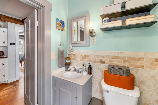 half bath featuring toilet, wood finished floors, vanity, tile walls, and wainscoting