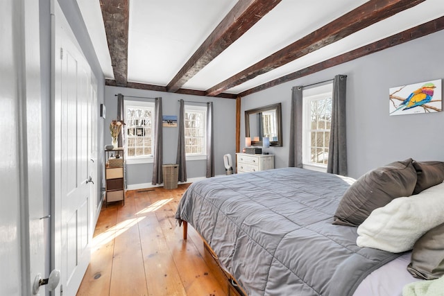 bedroom featuring light wood finished floors, baseboards, and beamed ceiling