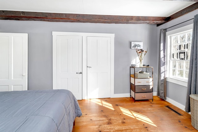 bedroom with light wood-type flooring, baseboards, visible vents, and beamed ceiling