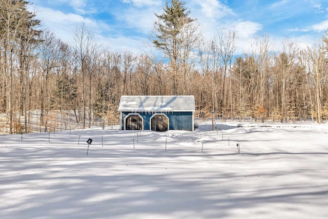 snow covered structure with a forest view, an outdoor structure, and a barn