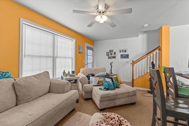 living room featuring ceiling fan, stairs, baseboards, and light colored carpet