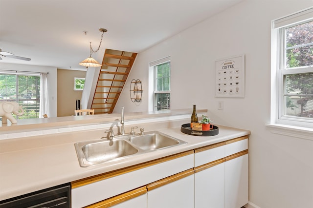 kitchen with a sink, white cabinets, black dishwasher, light countertops, and hanging light fixtures