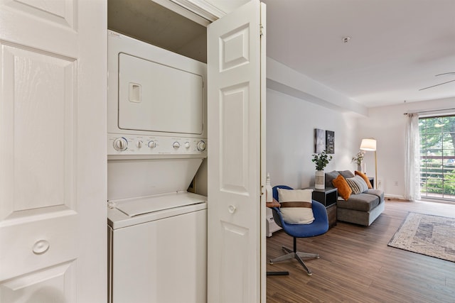 laundry area featuring stacked washer and clothes dryer, a baseboard heating unit, wood finished floors, laundry area, and baseboards