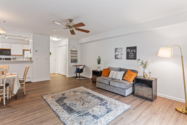 living area featuring a baseboard heating unit, ceiling fan, baseboards, and wood finished floors