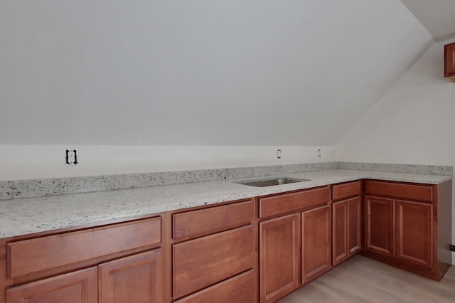 kitchen featuring lofted ceiling, light stone counters, brown cabinets, light wood-type flooring, and a sink