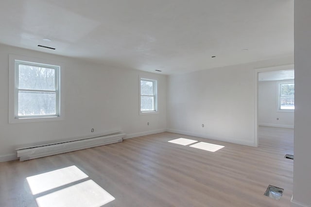 empty room featuring light wood-type flooring, a baseboard radiator, and a healthy amount of sunlight