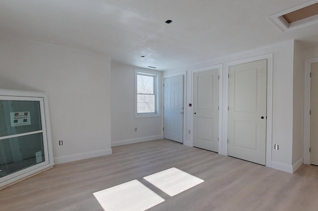 unfurnished bedroom with light wood-type flooring, attic access, baseboards, and two closets