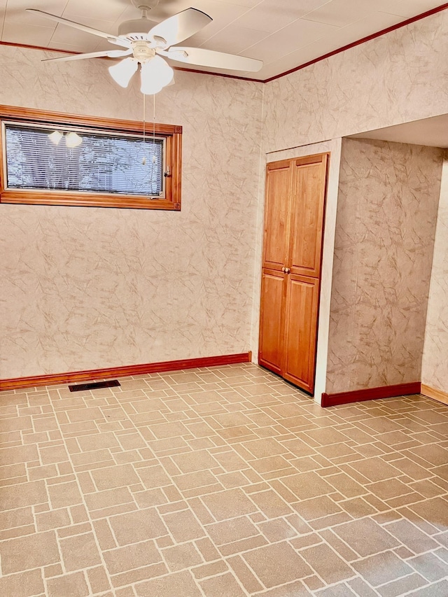 empty room with brick floor, visible vents, baseboards, and ceiling fan