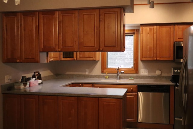 kitchen featuring brown cabinetry, appliances with stainless steel finishes, a peninsula, and a sink