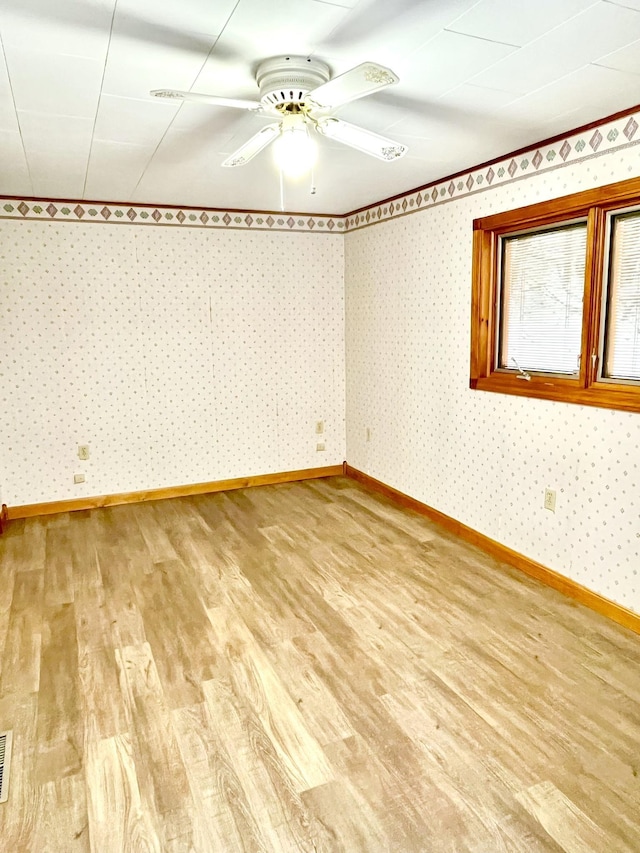 empty room featuring wallpapered walls, wood finished floors, baseboards, and ceiling fan