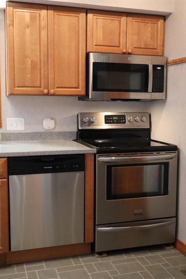 kitchen with brick floor, stainless steel appliances, baseboards, and light countertops