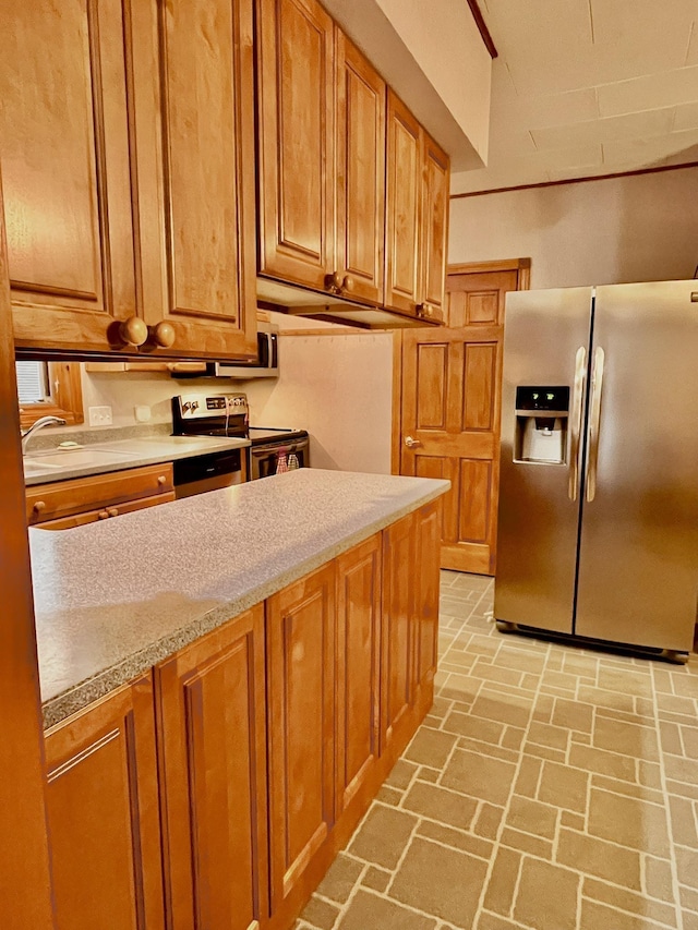 kitchen featuring brown cabinetry, brick floor, a sink, stainless steel appliances, and light countertops