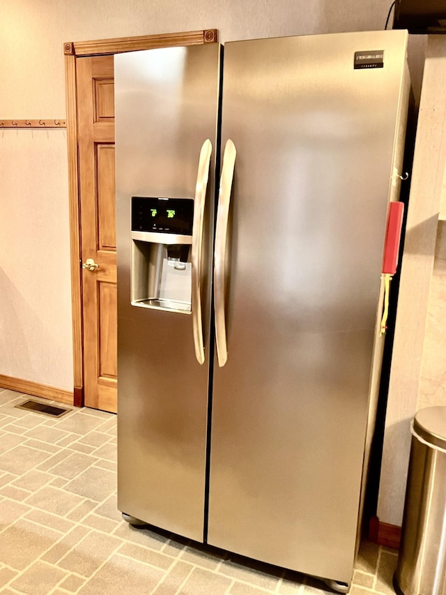 details featuring baseboards, stainless steel fridge, visible vents, and brown cabinetry