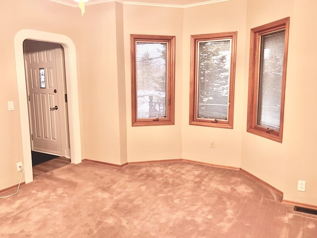 carpeted empty room featuring visible vents, arched walkways, baseboards, and ornamental molding