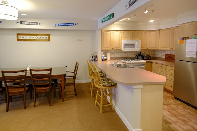 kitchen featuring light brown cabinetry, light countertops, white microwave, and freestanding refrigerator