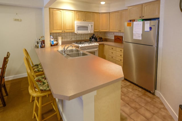 kitchen featuring white appliances, light brown cabinets, a peninsula, and a breakfast bar area