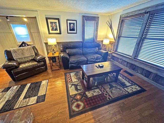 living room with wooden walls, a wainscoted wall, a textured ceiling, and wood finished floors