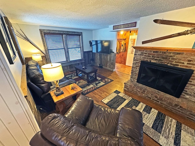 living area with a brick fireplace, wainscoting, wood walls, a textured ceiling, and wood finished floors