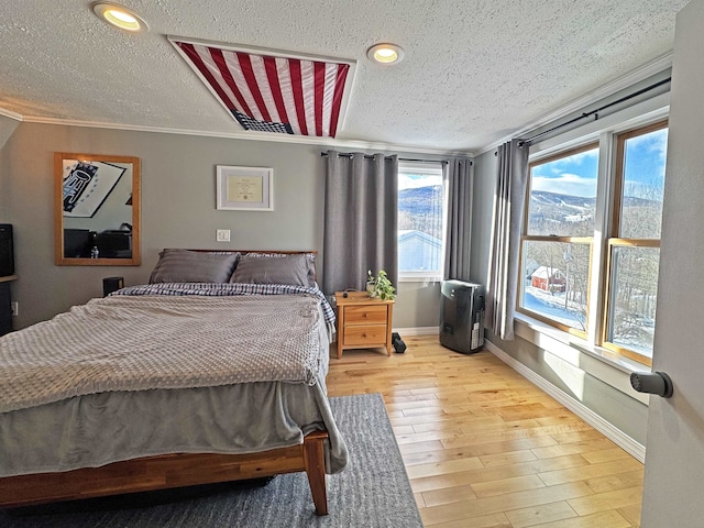 bedroom featuring a textured ceiling, ornamental molding, light wood-style flooring, and baseboards