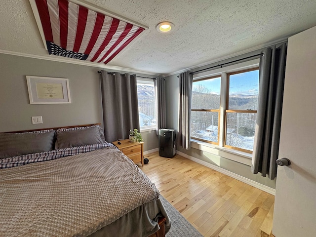 bedroom with a textured ceiling, crown molding, wood finished floors, and baseboards