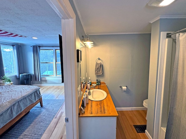 interior space with crown molding, visible vents, vanity, wood finished floors, and baseboards