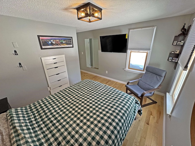 bedroom with baseboards, light wood-style flooring, and a textured ceiling