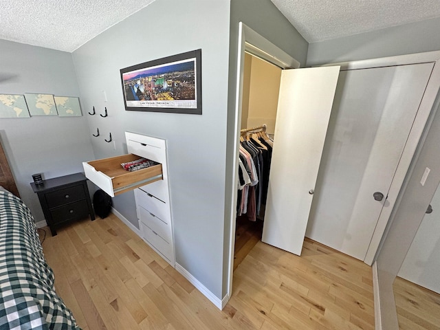 bedroom with a textured ceiling, a closet, light wood-style flooring, and baseboards