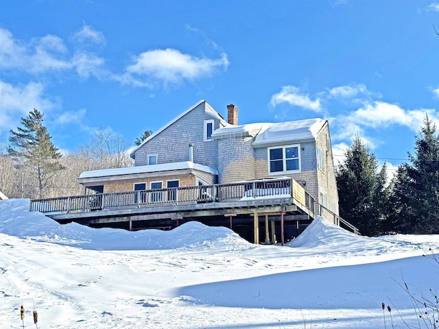 snow covered house with a chimney and a wooden deck