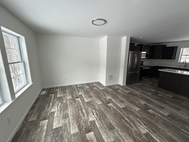 unfurnished living room with dark wood-style floors, a sink, visible vents, and baseboards