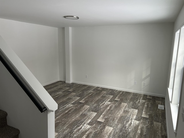 empty room featuring dark wood-style flooring, visible vents, stairway, and baseboards