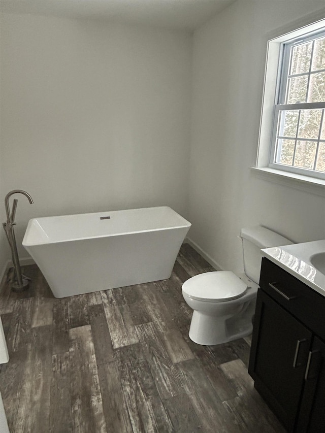 bathroom featuring a freestanding bath, toilet, wood finished floors, and vanity