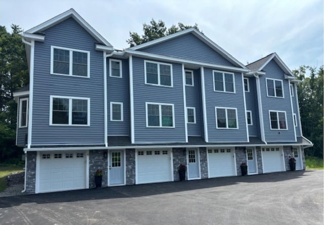 view of property with an attached garage, driveway, and stone siding