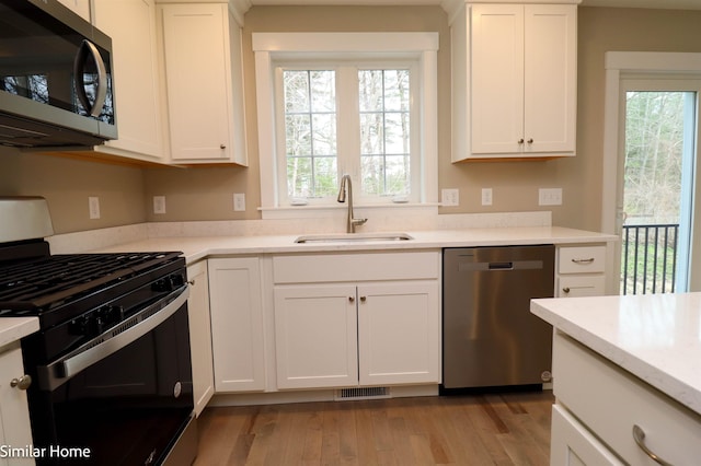 kitchen with stainless steel appliances, a sink, white cabinetry, light countertops, and light wood finished floors