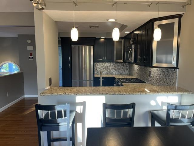 kitchen with stainless steel appliances, light stone countertops, a peninsula, and tasteful backsplash