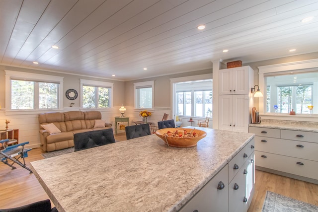 kitchen featuring light stone counters, wooden ceiling, white cabinetry, open floor plan, and wainscoting