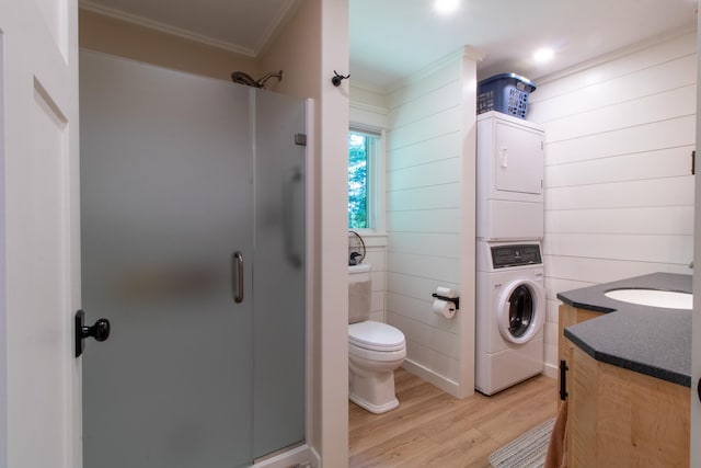 full bathroom with a stall shower, stacked washer and clothes dryer, wood finished floors, crown molding, and vanity