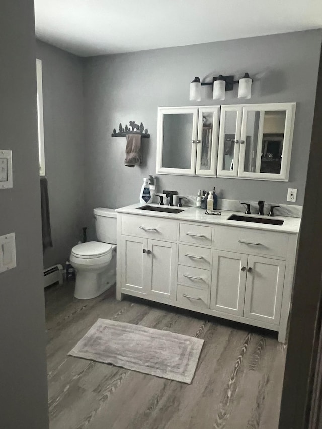 bathroom with toilet, baseboard heating, a sink, and wood finished floors