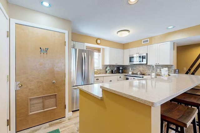 kitchen with white cabinets, appliances with stainless steel finishes, a peninsula, light countertops, and a kitchen bar