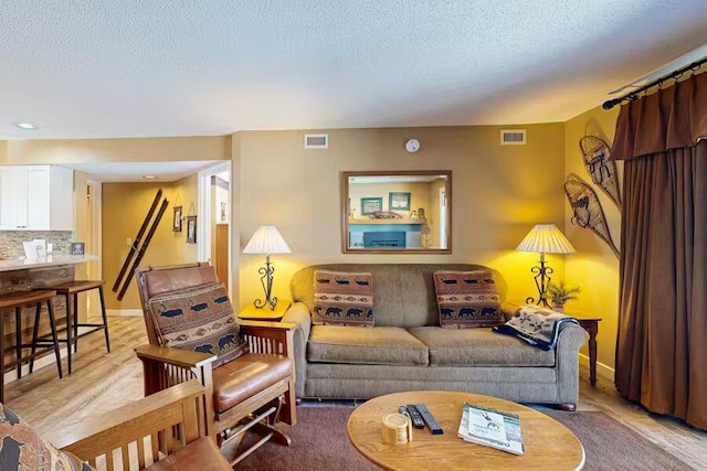 living area featuring light wood-type flooring, visible vents, a textured ceiling, and baseboards