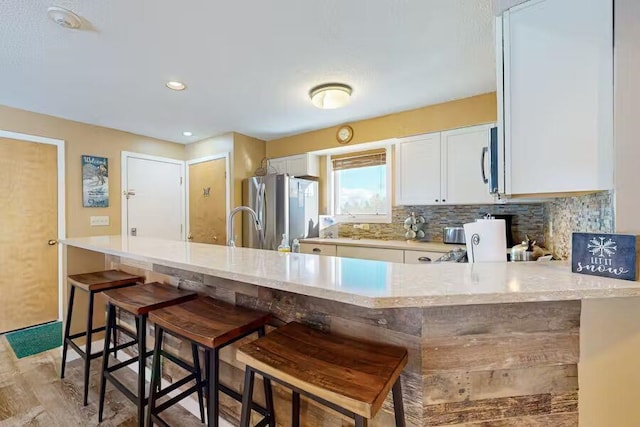 kitchen with white cabinets, appliances with stainless steel finishes, a peninsula, a kitchen bar, and backsplash