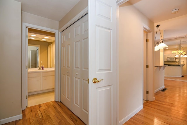 corridor featuring baseboards, visible vents, a sink, and light wood finished floors