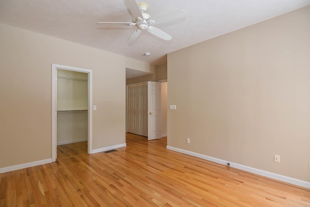 unfurnished bedroom featuring a walk in closet, a closet, visible vents, light wood-style flooring, and baseboards