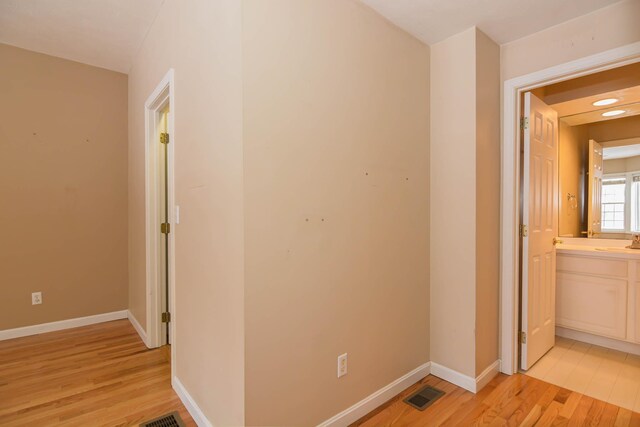 corridor featuring baseboards, visible vents, a sink, and light wood finished floors