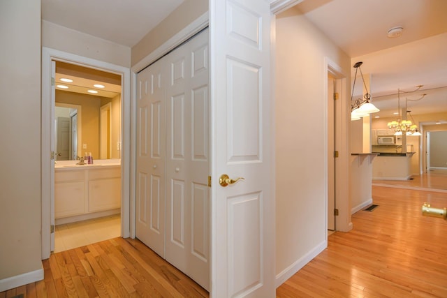 corridor with light wood-type flooring, a sink, visible vents, and baseboards