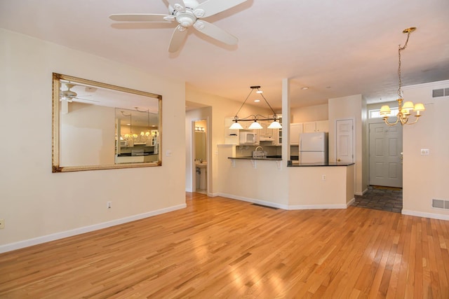 unfurnished living room featuring light wood-style floors, visible vents, baseboards, and ceiling fan with notable chandelier