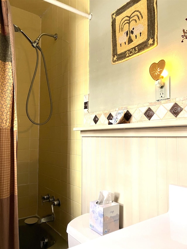 bathroom featuring toilet, shower / bath combo, and wainscoting