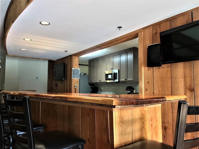 kitchen featuring stainless steel microwave, a kitchen breakfast bar, backsplash, and recessed lighting