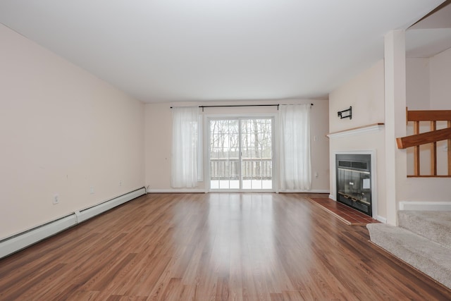 unfurnished living room featuring baseboards, a baseboard heating unit, wood finished floors, and a glass covered fireplace